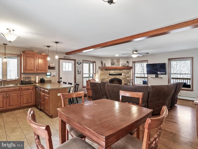 dining room featuring beamed ceiling, a ceiling fan, a stone fireplace, light tile patterned floors, and baseboard heating