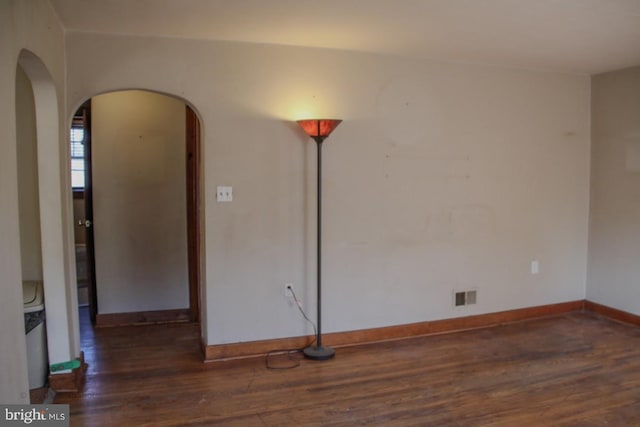 empty room featuring visible vents, wood finished floors, arched walkways, and baseboards