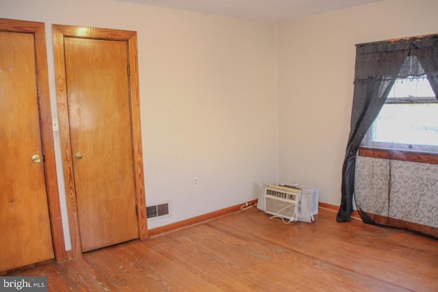 unfurnished room featuring visible vents, baseboards, wood finished floors, and a wall unit AC