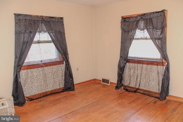 empty room featuring visible vents, a healthy amount of sunlight, and wood finished floors