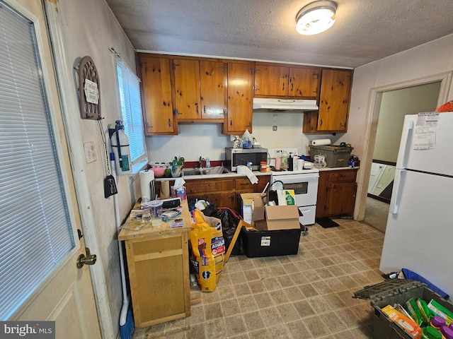 kitchen featuring under cabinet range hood, brown cabinets, white appliances, a textured ceiling, and a sink