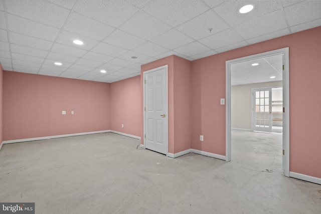 spare room featuring a drop ceiling, recessed lighting, baseboards, and concrete flooring