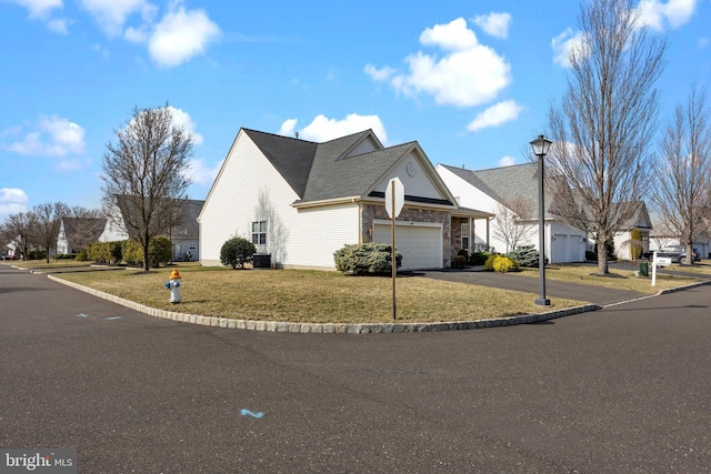 view of front of property with a front yard, central AC unit, an attached garage, stone siding, and aphalt driveway