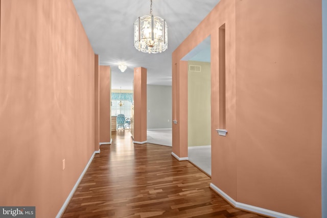 corridor featuring baseboards, wood finished floors, visible vents, and a chandelier