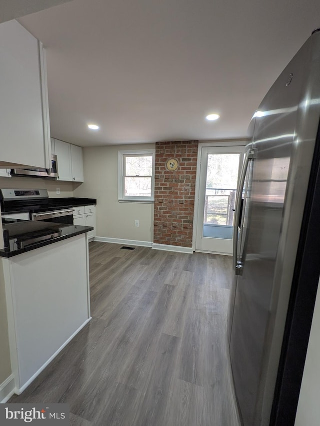 kitchen featuring dark countertops, wood finished floors, white cabinetry, stainless steel appliances, and baseboards