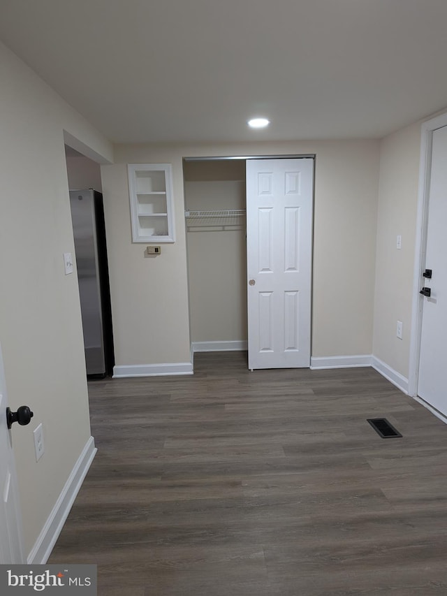 unfurnished bedroom featuring dark wood-style floors, visible vents, freestanding refrigerator, and baseboards