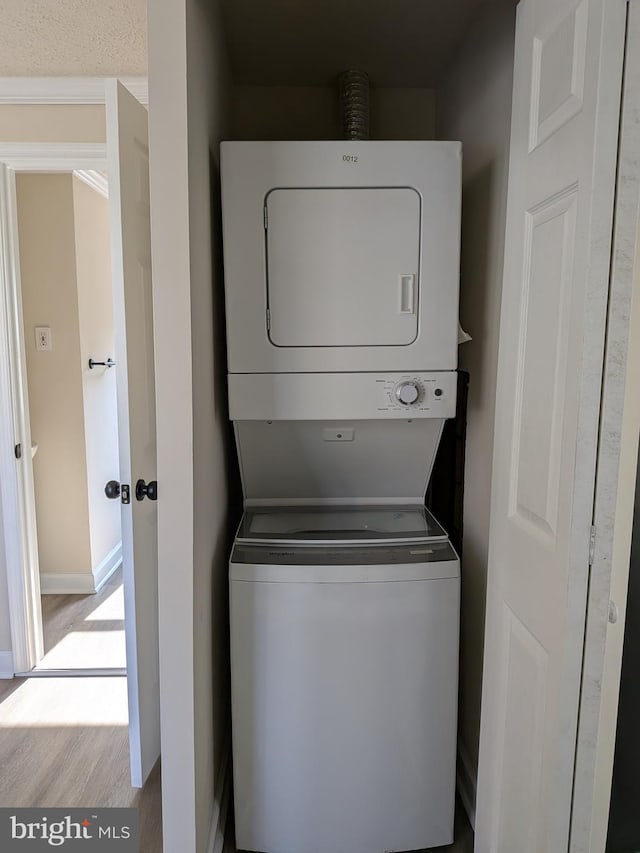 laundry room featuring stacked washer / dryer, wood finished floors, and baseboards