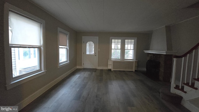 unfurnished living room with dark wood-style floors, stairway, a fireplace, and a wealth of natural light