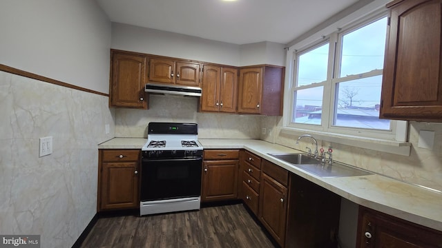 kitchen featuring dark wood-type flooring, under cabinet range hood, a sink, gas range oven, and light countertops