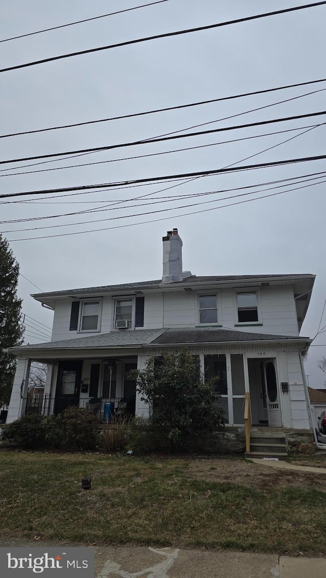 view of front facade with covered porch, a chimney, and a front yard