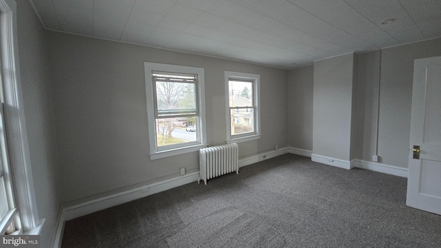 unfurnished room featuring baseboards, dark carpet, and radiator heating unit