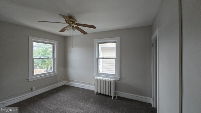 spare room featuring dark carpet, radiator, baseboards, and ceiling fan