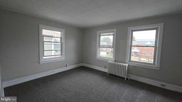 unfurnished room featuring dark carpet, radiator heating unit, and baseboards