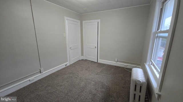 spare room featuring dark carpet, crown molding, and radiator heating unit