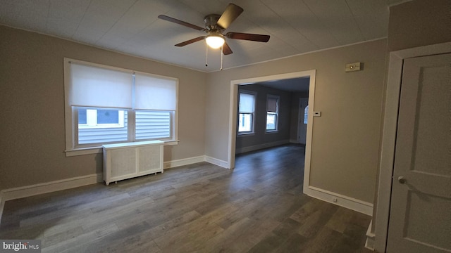 empty room featuring dark wood finished floors, radiator, baseboards, and ceiling fan