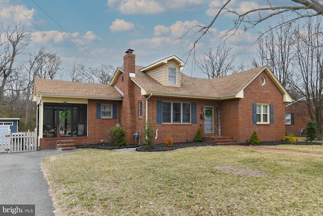 view of front facade featuring fence, a front yard, a shingled roof, brick siding, and a chimney