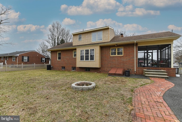 back of property with central air condition unit, fence, a yard, a fire pit, and brick siding