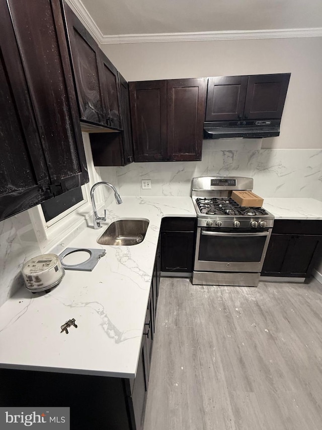 kitchen with crown molding, light stone countertops, under cabinet range hood, stainless steel gas range, and a sink