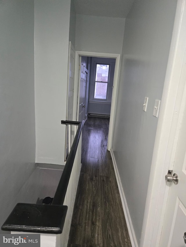 corridor featuring an upstairs landing, baseboard heating, baseboards, and dark wood-style flooring