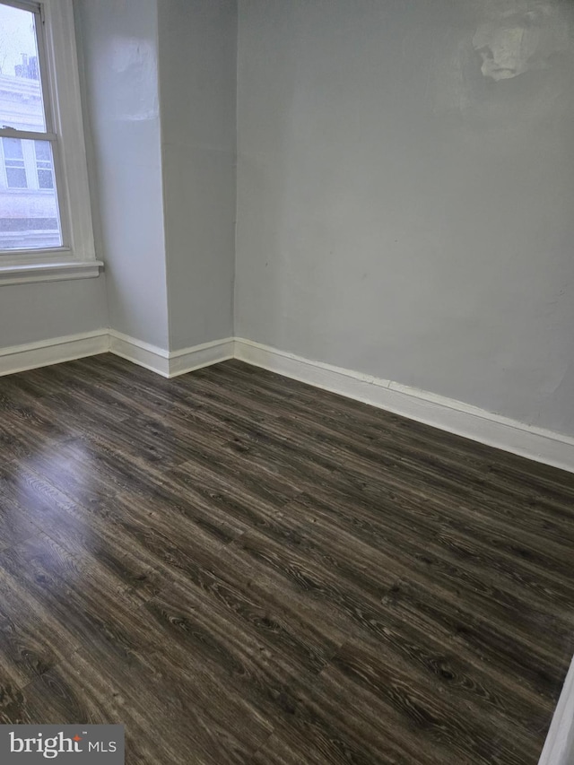 spare room with baseboards and dark wood-style flooring