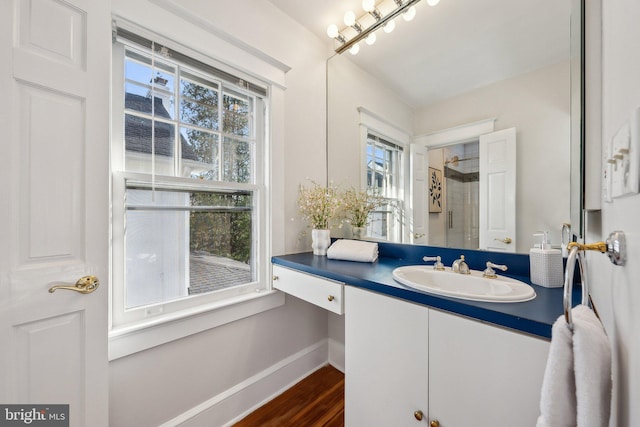 bathroom with vanity, wood finished floors, baseboards, and a tile shower