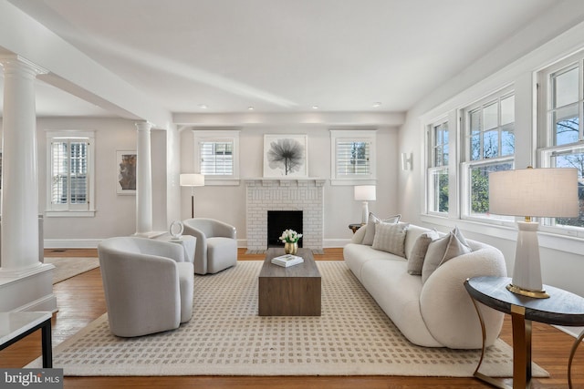 living room featuring decorative columns, baseboards, a brick fireplace, and wood finished floors