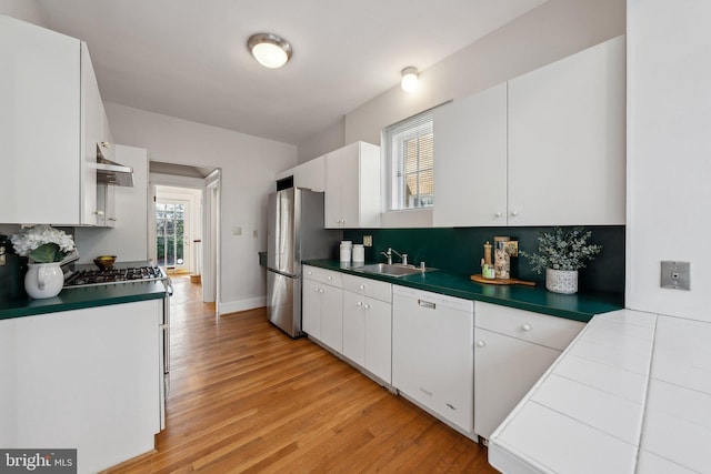 kitchen with a sink, white cabinetry, light wood-style floors, appliances with stainless steel finishes, and wall chimney exhaust hood