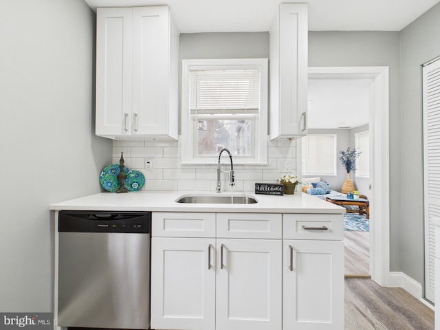 kitchen featuring a sink, light countertops, white cabinets, stainless steel dishwasher, and tasteful backsplash