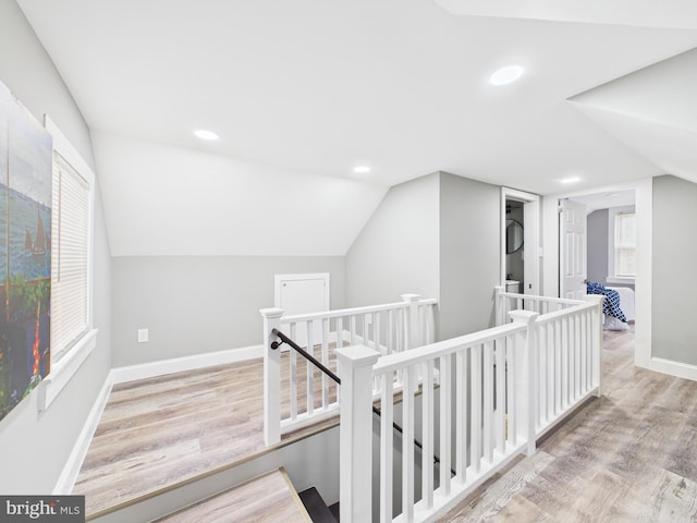 hall with baseboards, an upstairs landing, lofted ceiling, and wood finished floors