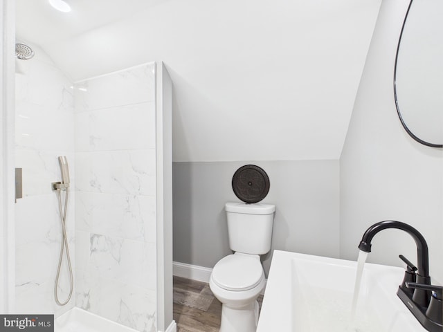 full bathroom featuring toilet, a sink, wood finished floors, tiled shower, and vaulted ceiling