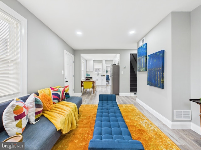 living area with light wood finished floors, visible vents, stairs, and baseboards