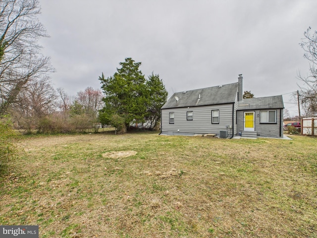 back of house with central AC unit, entry steps, a chimney, and a yard