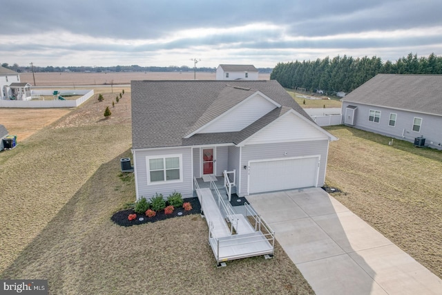 view of front of property with central AC unit, driveway, a shingled roof, a front lawn, and a garage