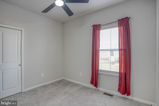 carpeted spare room featuring baseboards, visible vents, a wealth of natural light, and ceiling fan