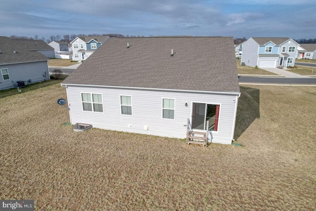 rear view of property featuring a yard, a residential view, and roof with shingles