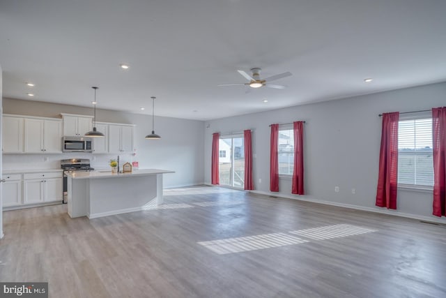 unfurnished living room with a wealth of natural light, baseboards, light wood-style flooring, and a ceiling fan