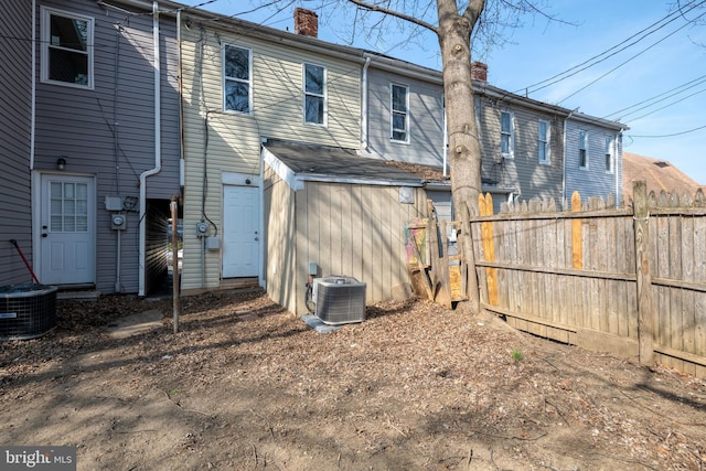 rear view of property featuring a chimney, central AC, and fence