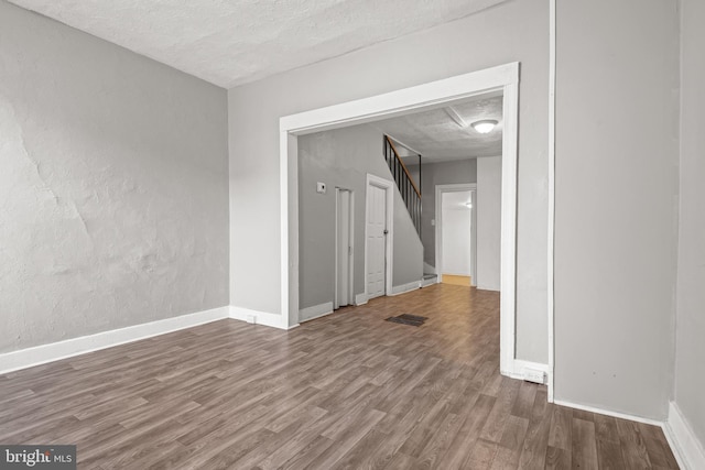 unfurnished room featuring stairway, wood finished floors, baseboards, and a textured ceiling