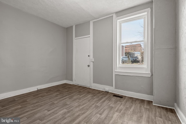 unfurnished room with baseboards, wood finished floors, visible vents, and a textured ceiling