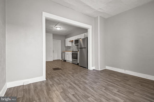 unfurnished living room featuring dark wood-style floors, a textured ceiling, baseboards, and a sink