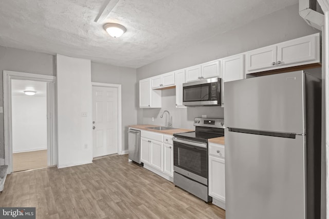 kitchen with appliances with stainless steel finishes, white cabinetry, light countertops, and a sink