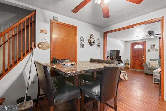 dining room with wood finished floors, a textured ceiling, ceiling fan, and stairs