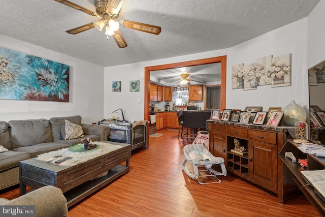 living area featuring a textured ceiling, light wood-type flooring, and a ceiling fan