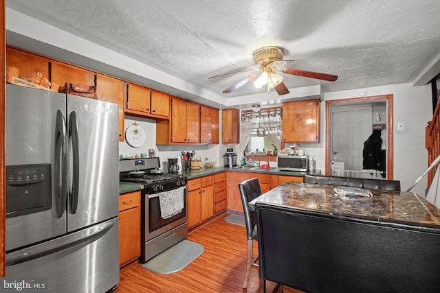 kitchen with dark countertops, ceiling fan, light wood-style floors, brown cabinetry, and stainless steel appliances