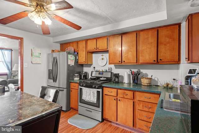 kitchen with dark countertops, ceiling fan, appliances with stainless steel finishes, light wood-style floors, and brown cabinetry