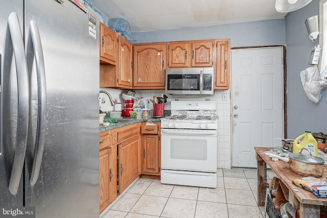 kitchen featuring light tile patterned floors, decorative backsplash, brown cabinetry, stainless steel appliances, and a sink