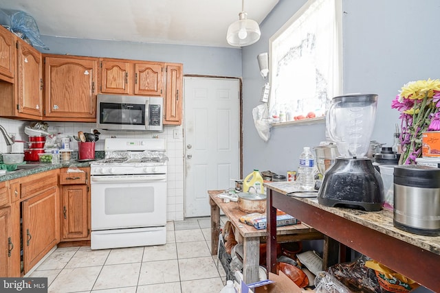 kitchen featuring white gas stove, a sink, stainless steel microwave, light tile patterned floors, and decorative backsplash