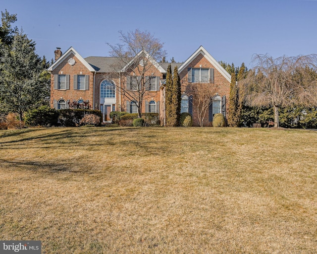 view of front of property with brick siding, a chimney, and a front lawn