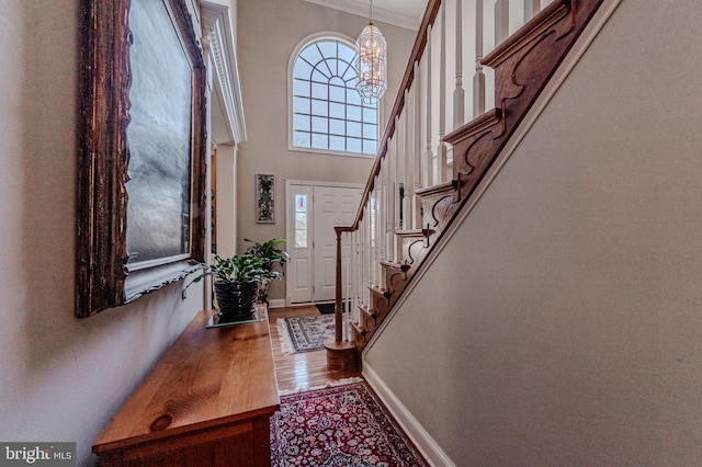 foyer entrance with crown molding, baseboards, a chandelier, stairs, and wood finished floors