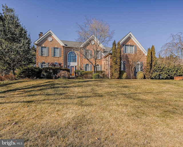 view of front of property with brick siding, a chimney, and a front yard